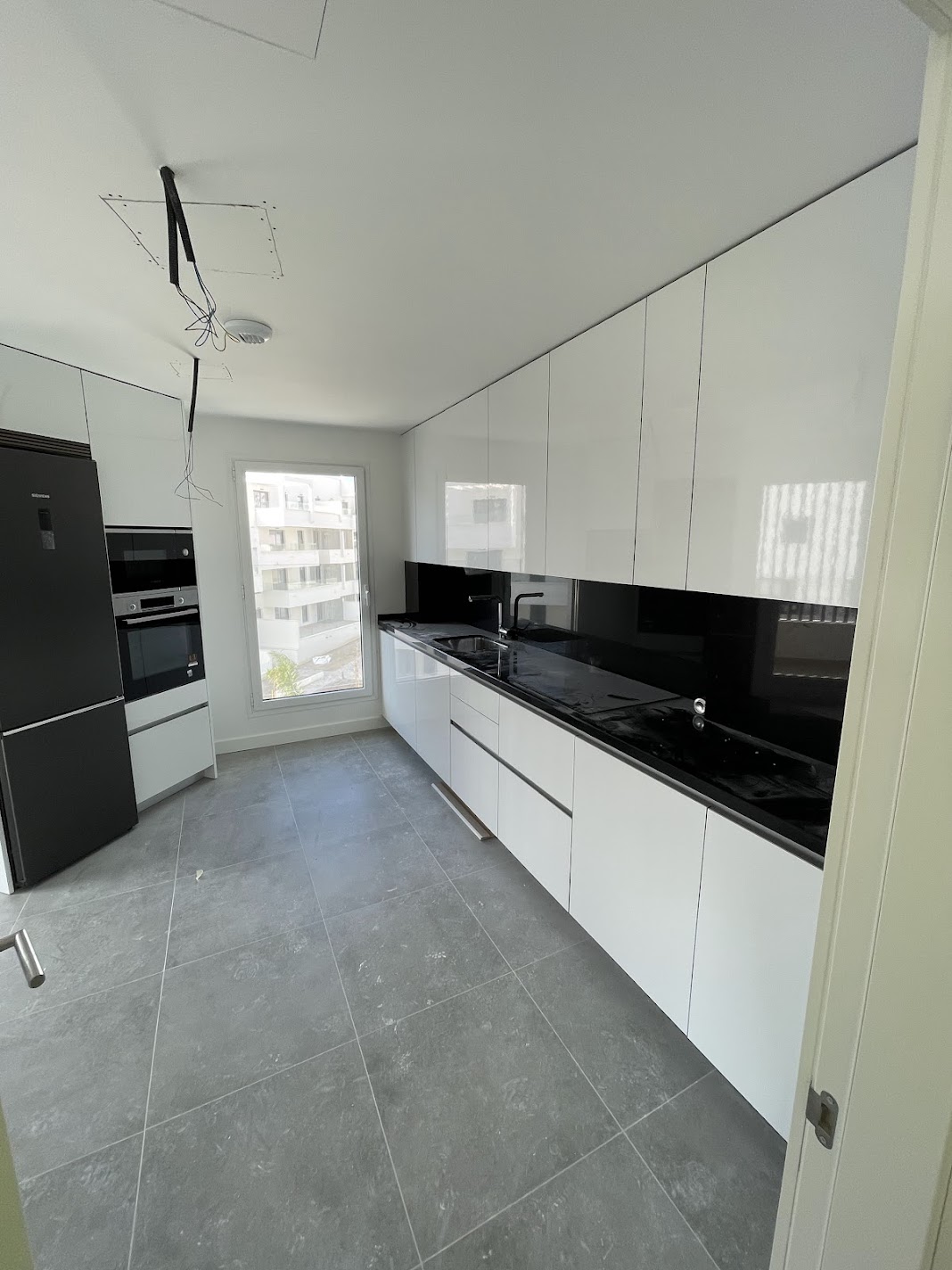 Reforma de cocina moderna blanca con encimera negra y suelo gris en Marbella - PintaPladur